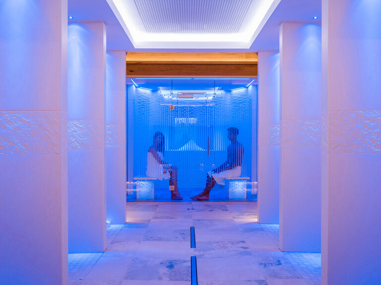 In der modern beleuchteten Sauna des Wellnesshotels Mooshof in Bayern erlebt ein Paar einen Moment der Regeneration.