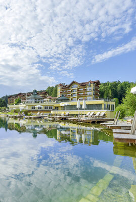 Der Blick auf das Hotel Mooshof über den glänzenden Naturbadesee.