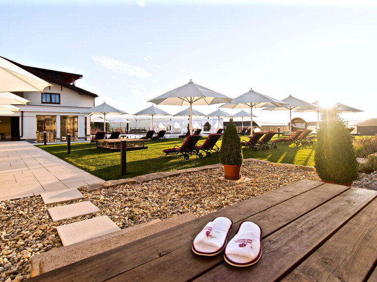 Die Außenanlage des Hotel Oswald in der Abendsonne mit zahlreichen roten Liegestühlen.